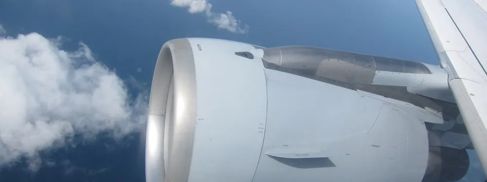 CFM56 engine under the wing of an Airbus A320 in flight, seen from a cabin window above clouds