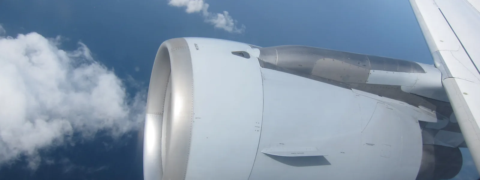 CFM56 engine under the wing of an Airbus A320 in flight, seen from a cabin window above clouds